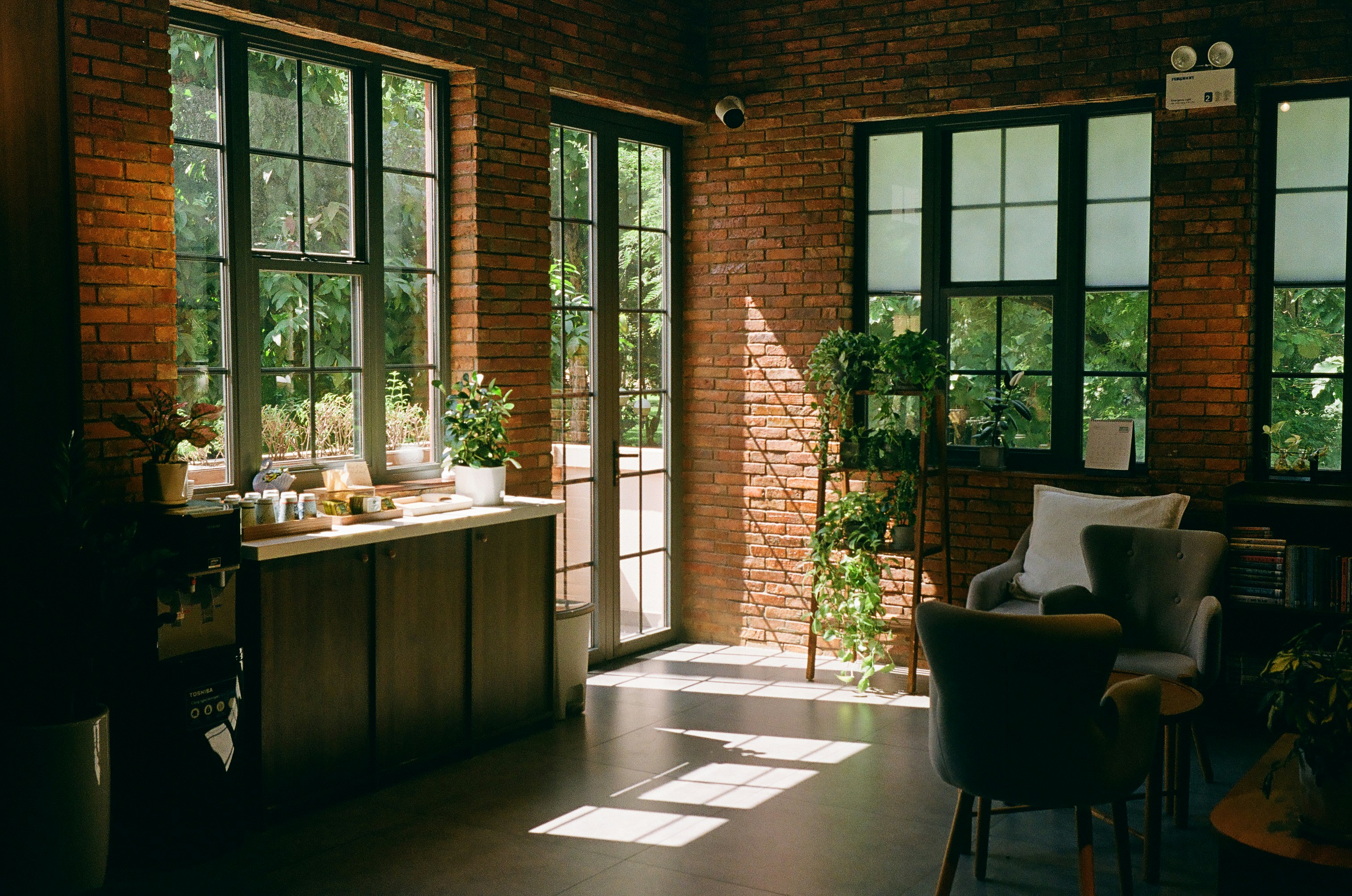 A daylight-filled interior with brick walls, windows, and plants.